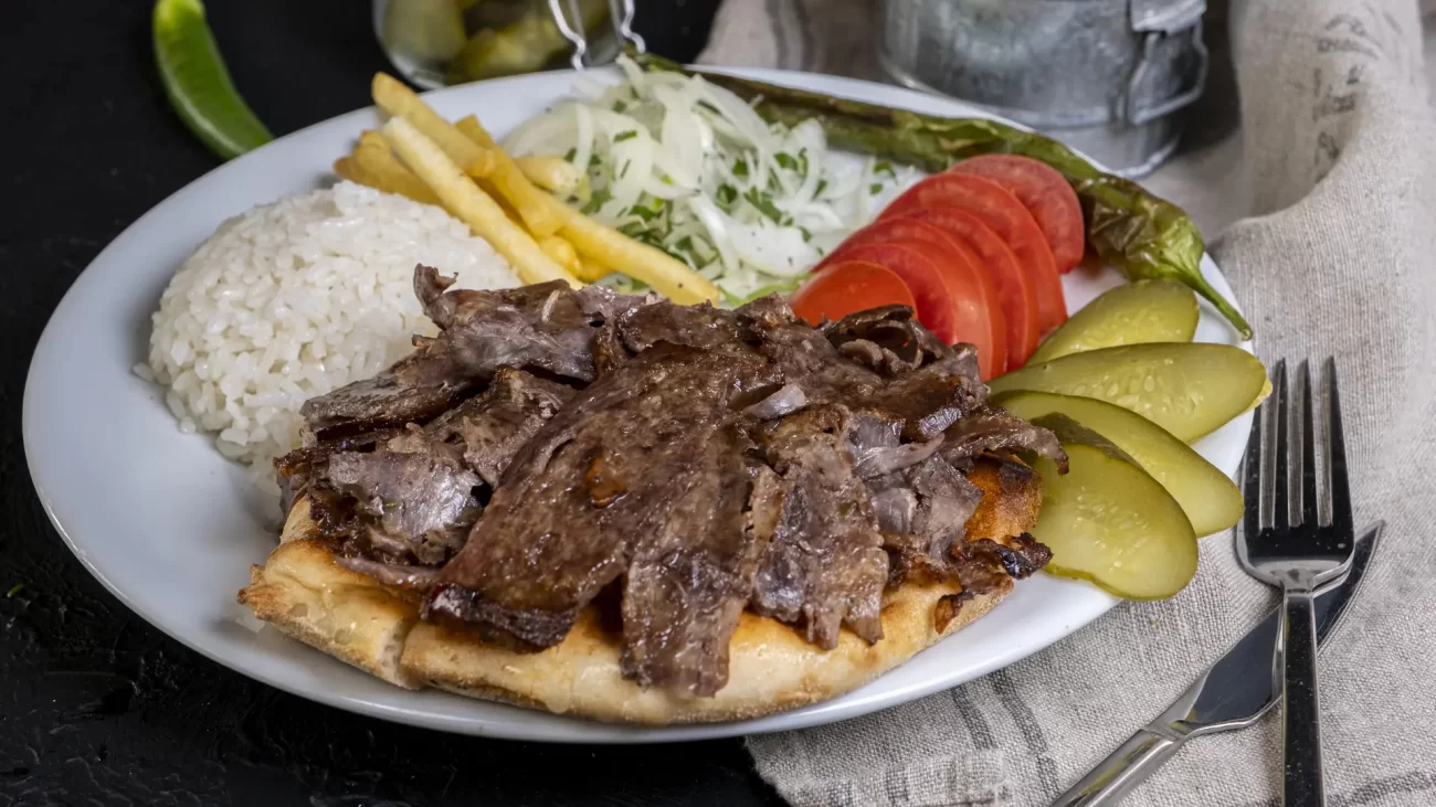 Taze pide üzerinde sunulan et döner, yanında pilav, turşu ve domates garnitürleriyle birlikte tabakta servis edilmiş.